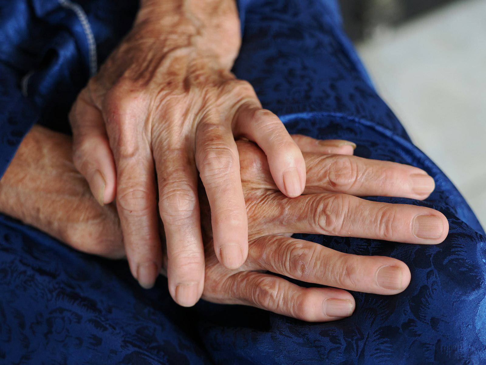 An older person's hands resting in a carer's hands
