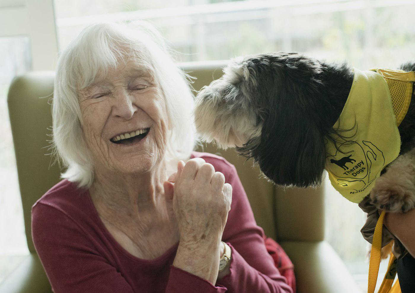 An older woman laughing as her dog leans in